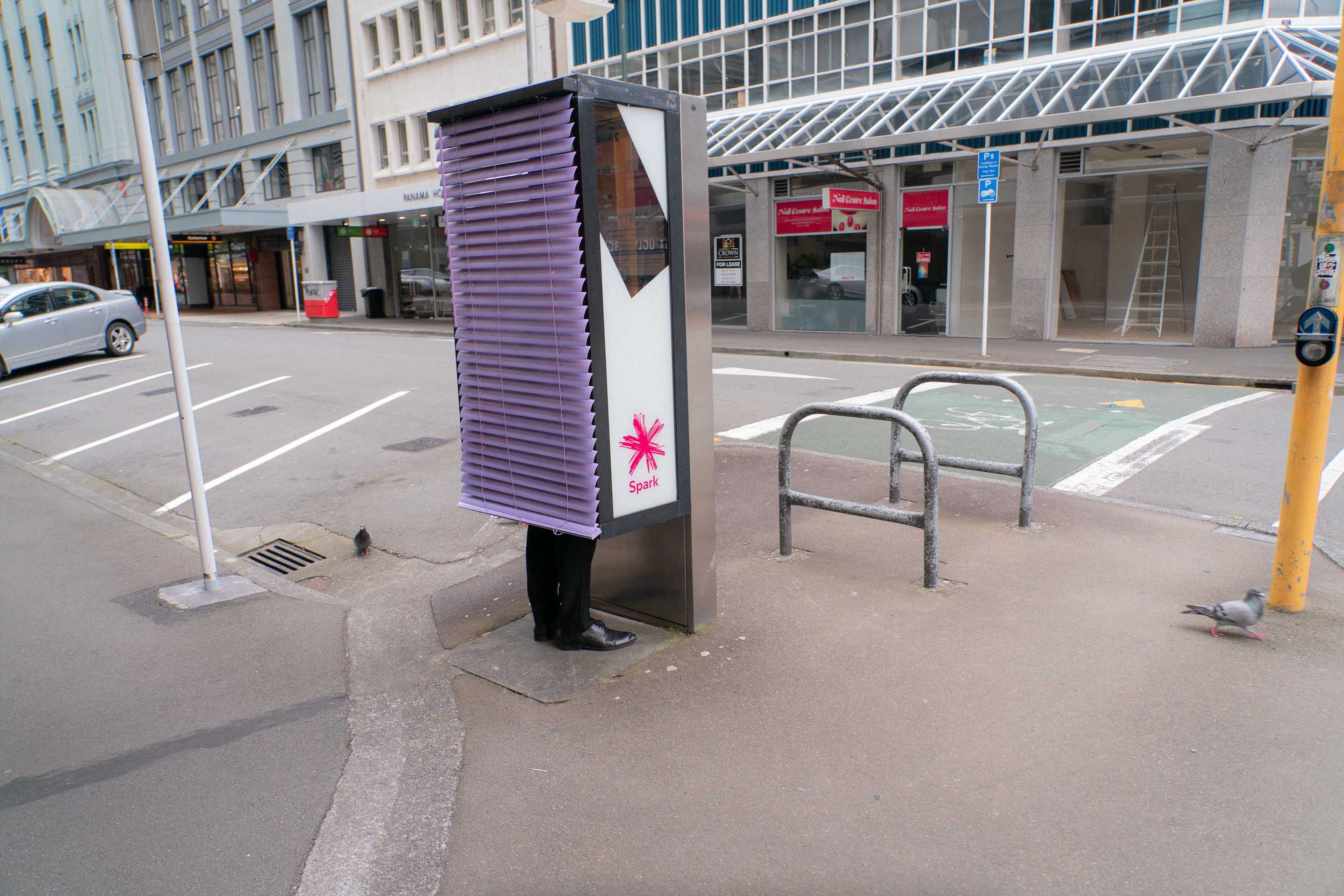 Street art installation by Cameron Hunt featuring purple Venetian blinds attached to a public phone booth.