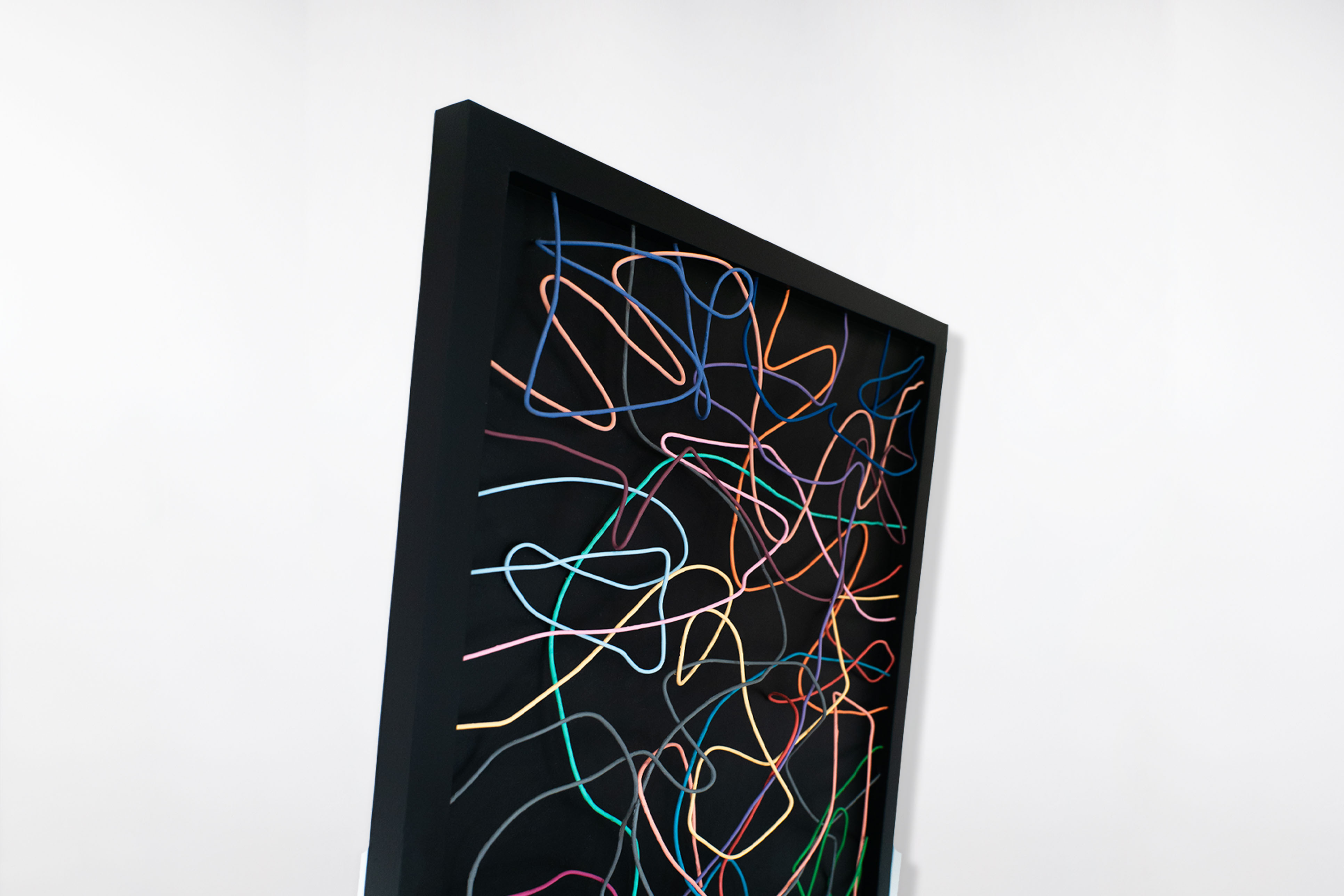 Side angle of a sculptural wall artwork by Cameron Hunt, featuring colourful interwoven lines looping across a deep black frame.