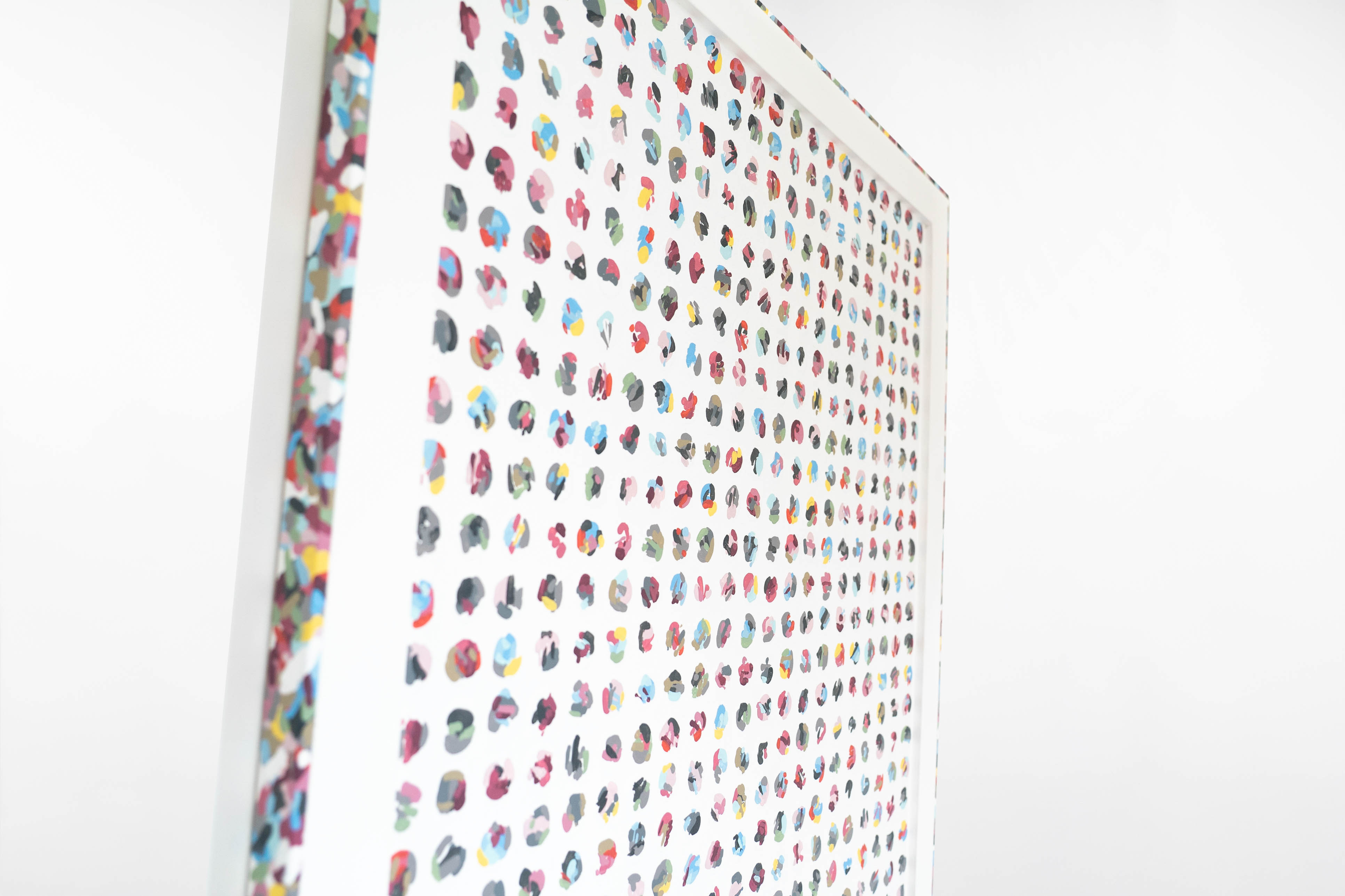 Angled close-up of a Cameron Hunt abstract painting, showing a grid of multicoloured circular dots on a white background. The framed edges matches the artwork’s palette.