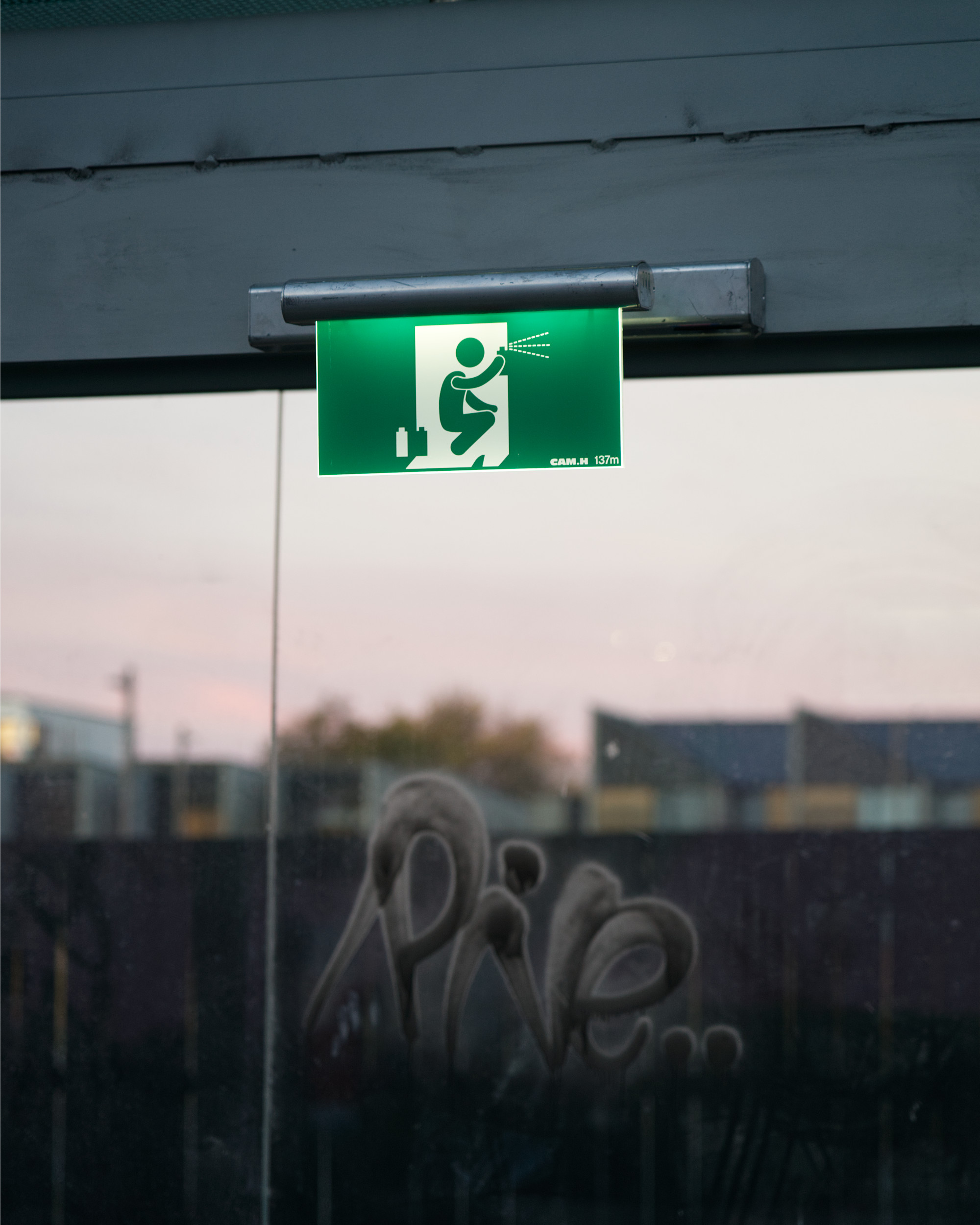 Refurbished illuminated exit sign featuring a running man figure spray-painted by street artist Cameron Hunt.