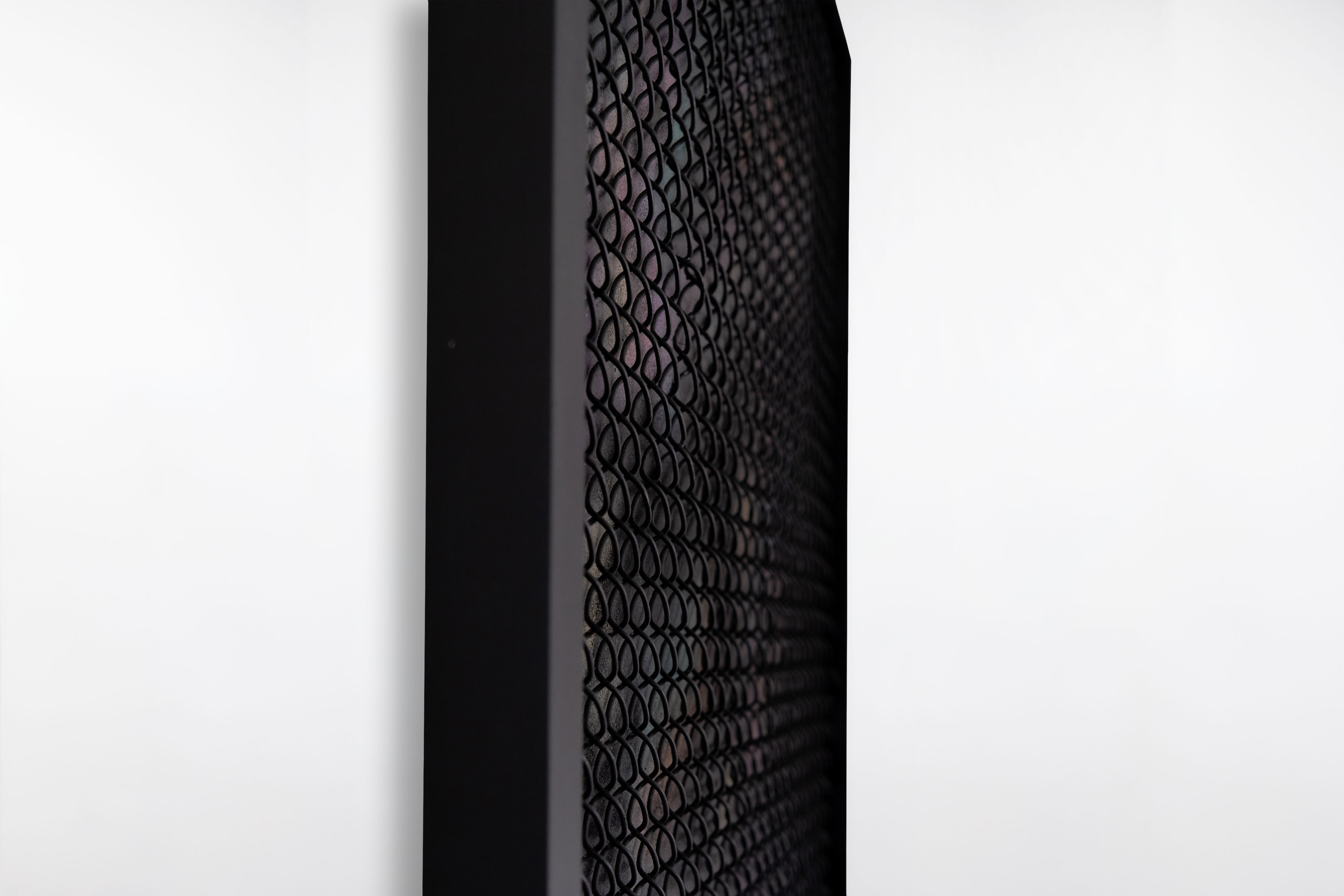 Side view of a framed painting by Cameron Hunt featuring a black metal mesh layer over a multicoloured, softly blurred background.