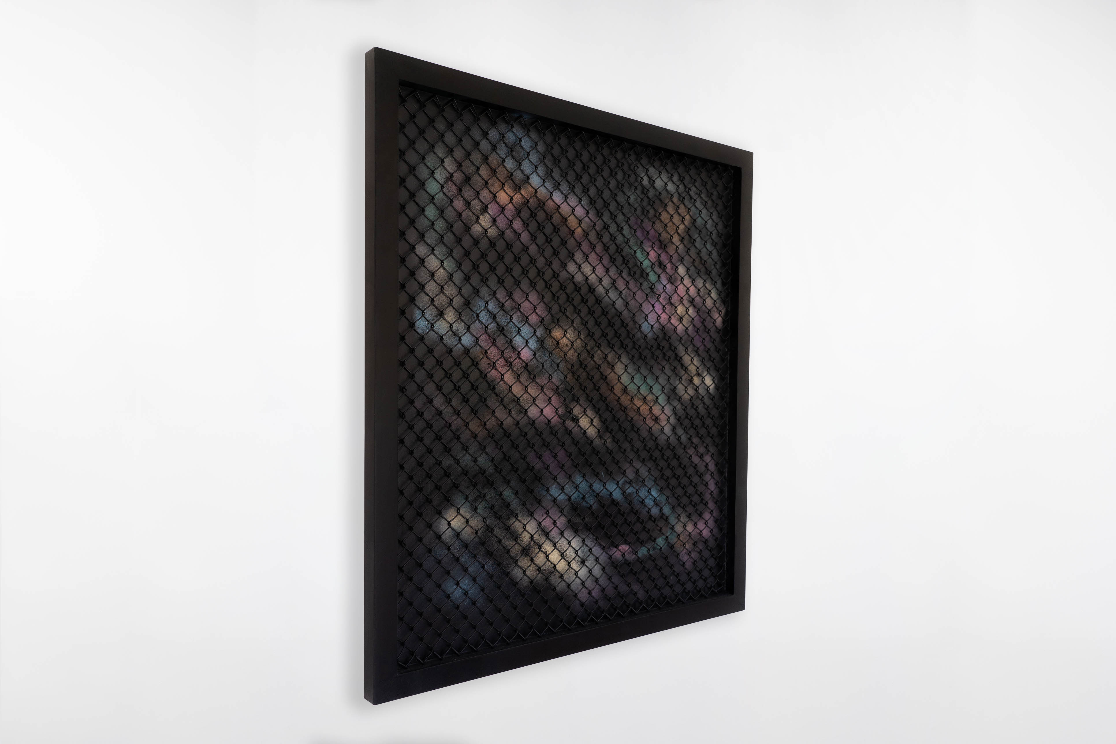 Angled view of a large framed painting by Cameron Hunt, with a black diamond mesh overlay in front of a spray-painted background. The underlying colours blend purples, blues, greens, and earthy tones beneath the structured surface.