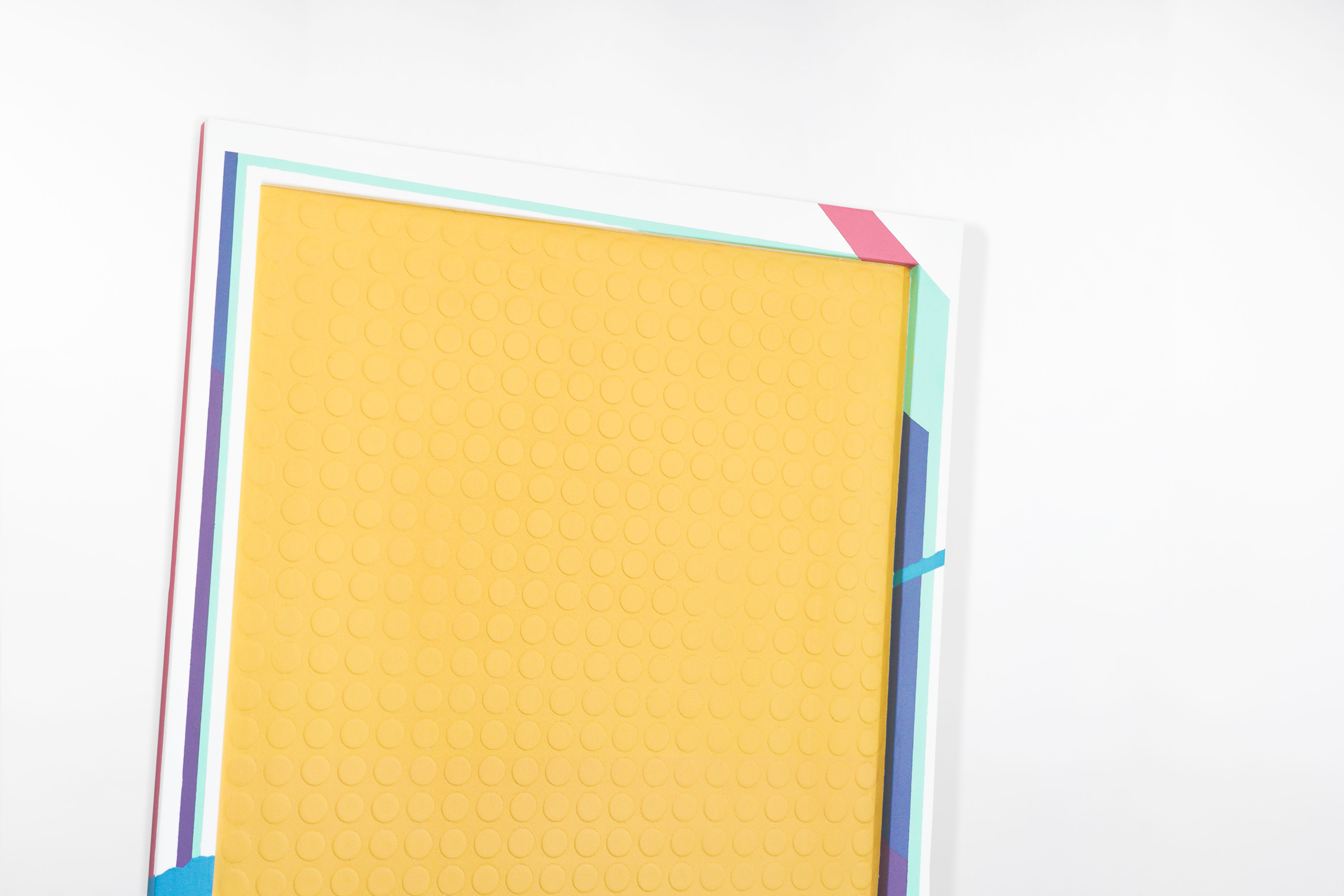 Close-up angled view of a contemporary abstract painting by Cameron Hunt, highlighting the textured yellow surface with raised circular patterns, framed by bold geometric borders in pink, teal, blue, and purple.