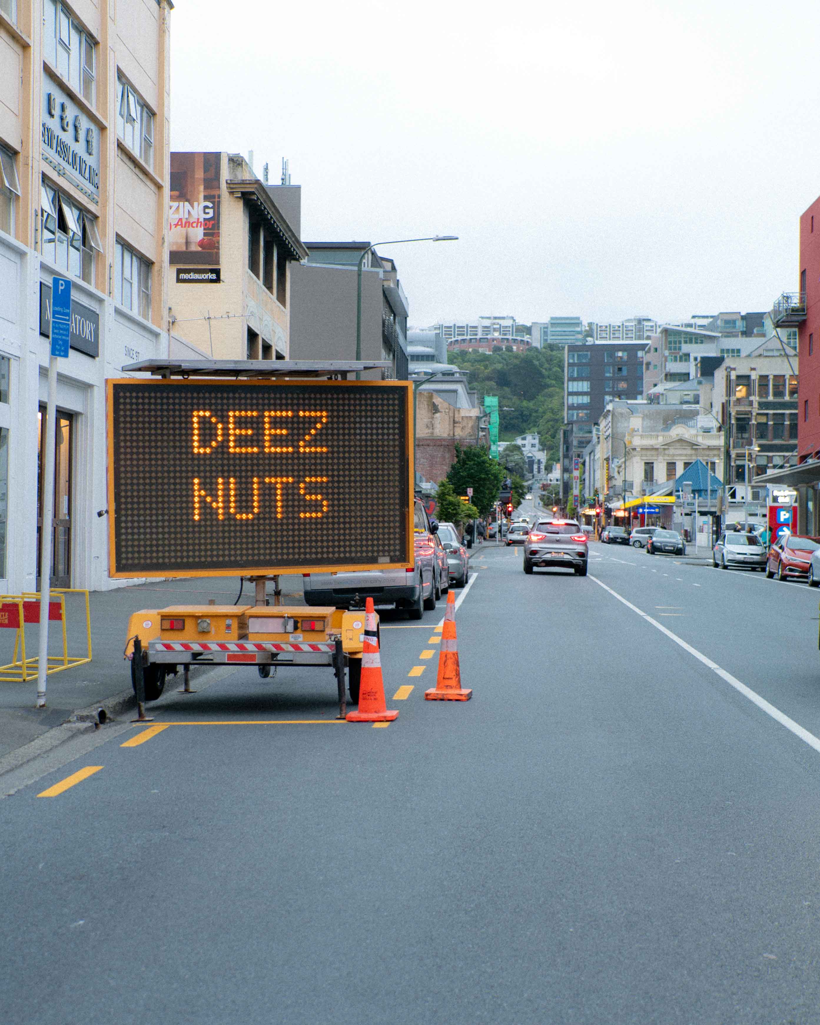 LED construction sign hacked to display the phrase "DEEZ NUTS" on a busy Wellington street, part of Cameron Hunt’s humorous street installation series.
