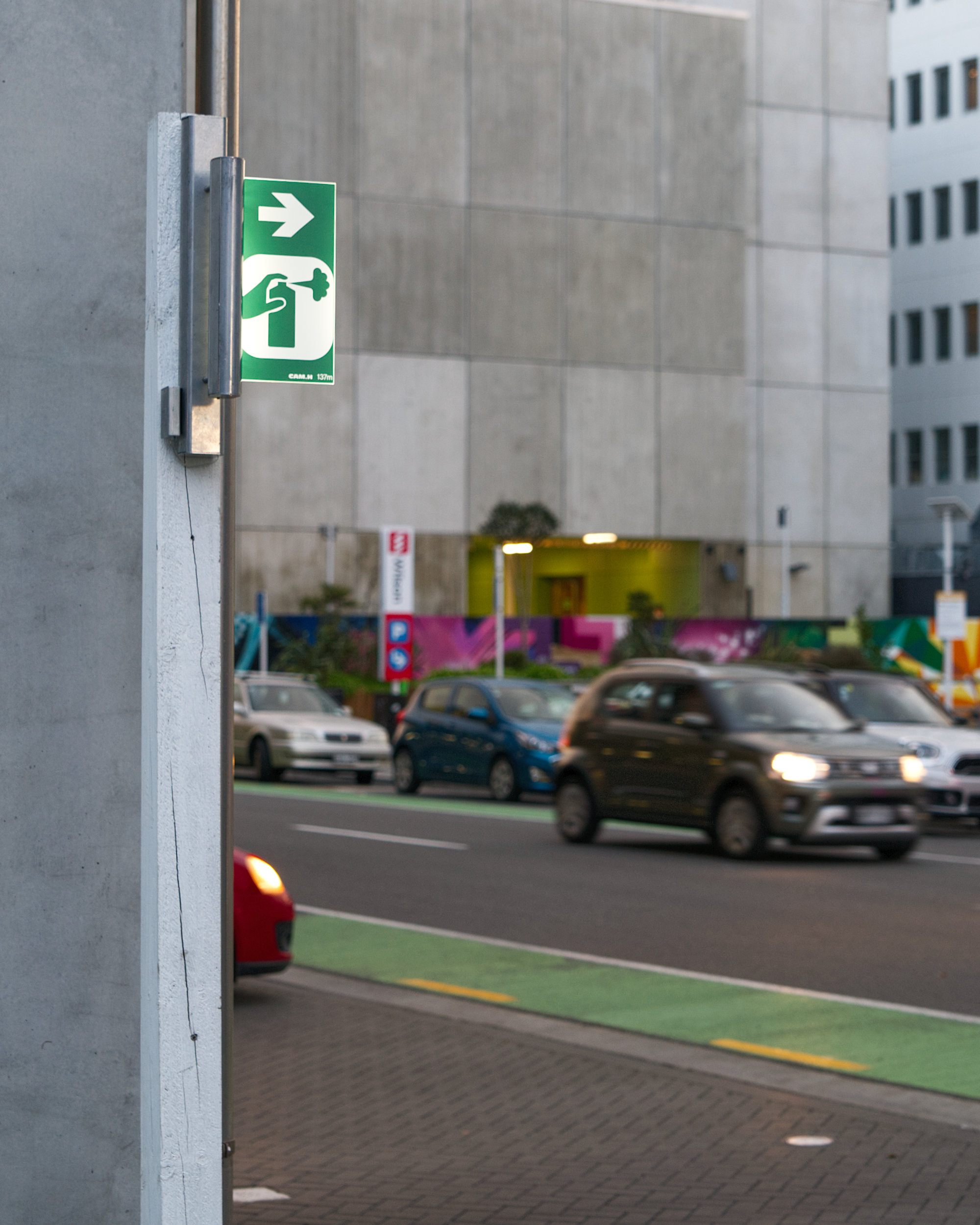 Illuminated exit sign redesigned with a hand holding a spray can and a right-pointing arrow symbolising movement toward the city and street art culture.
