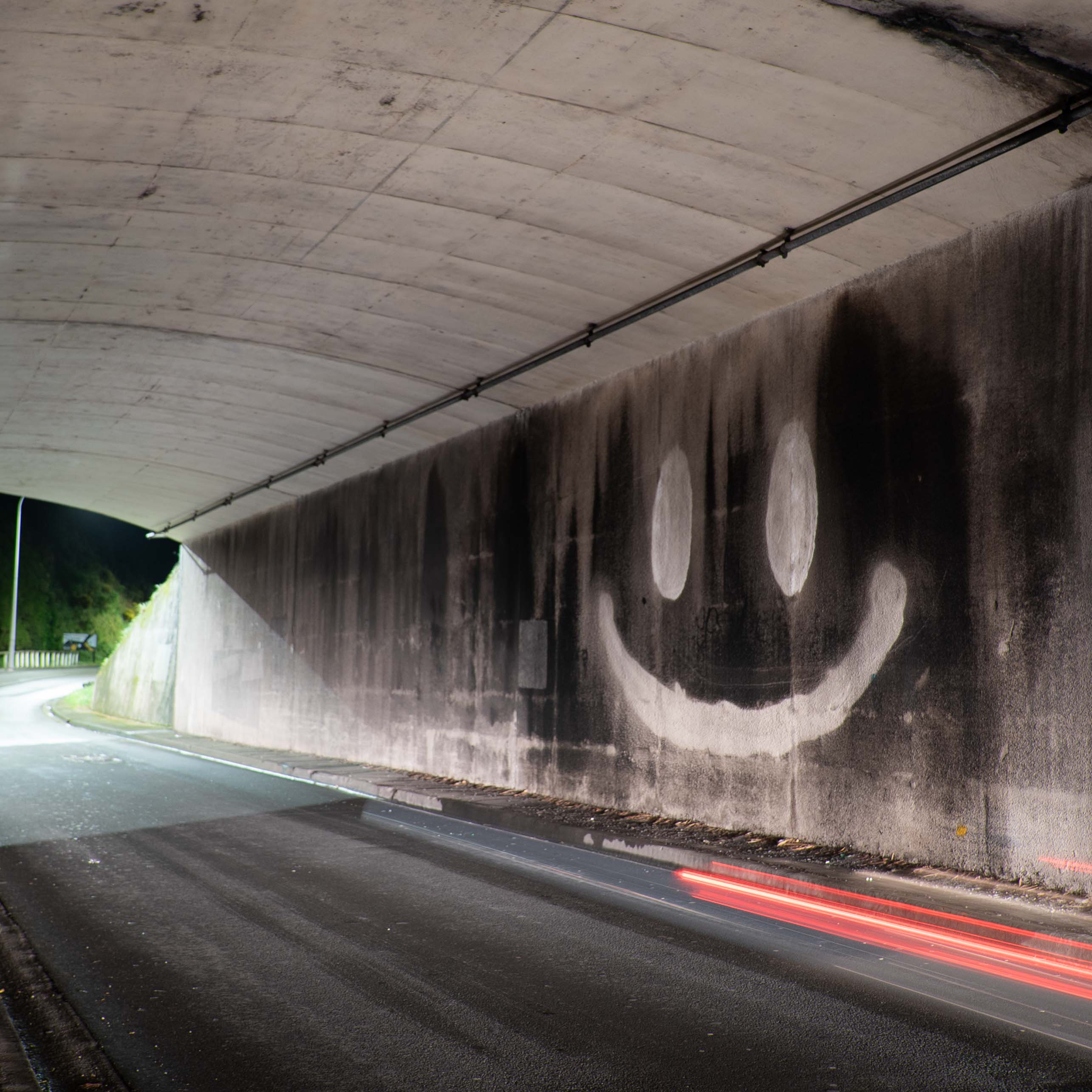Large smiley face created with reverse graffiti in a grimy urban tunnel by artist Cameron Hunt.
