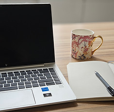 A laptop with notepad and a cup of tea