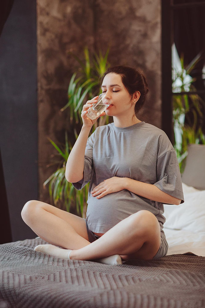 Pregnant woman enjoying a glass of pure water with her family nearby