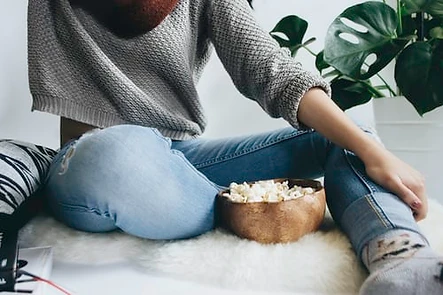 Woman sitting in jumper and skinny jeans eating popcorn.