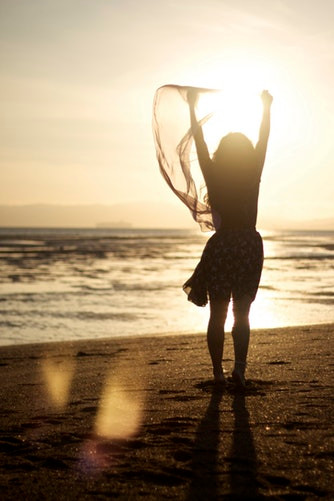 Woman standing on beach with arms in the air in celebration.