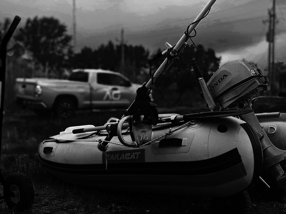 Bathymetry survey vessel on land in the foreground with single-beam echo sounders mounted, Aquaterra logo visible on the transom bracket; company pickup truck in soft focus in the background with matching Aquaterra logo on the side.