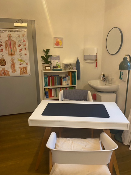 Arbeitsbereich in einer Heilpraktikerpraxis mit Schreibtisch, Bücher und Wandtafel. Heilpraktikerpraxis