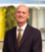 Smiling bald man in a dark suit and gold tie.