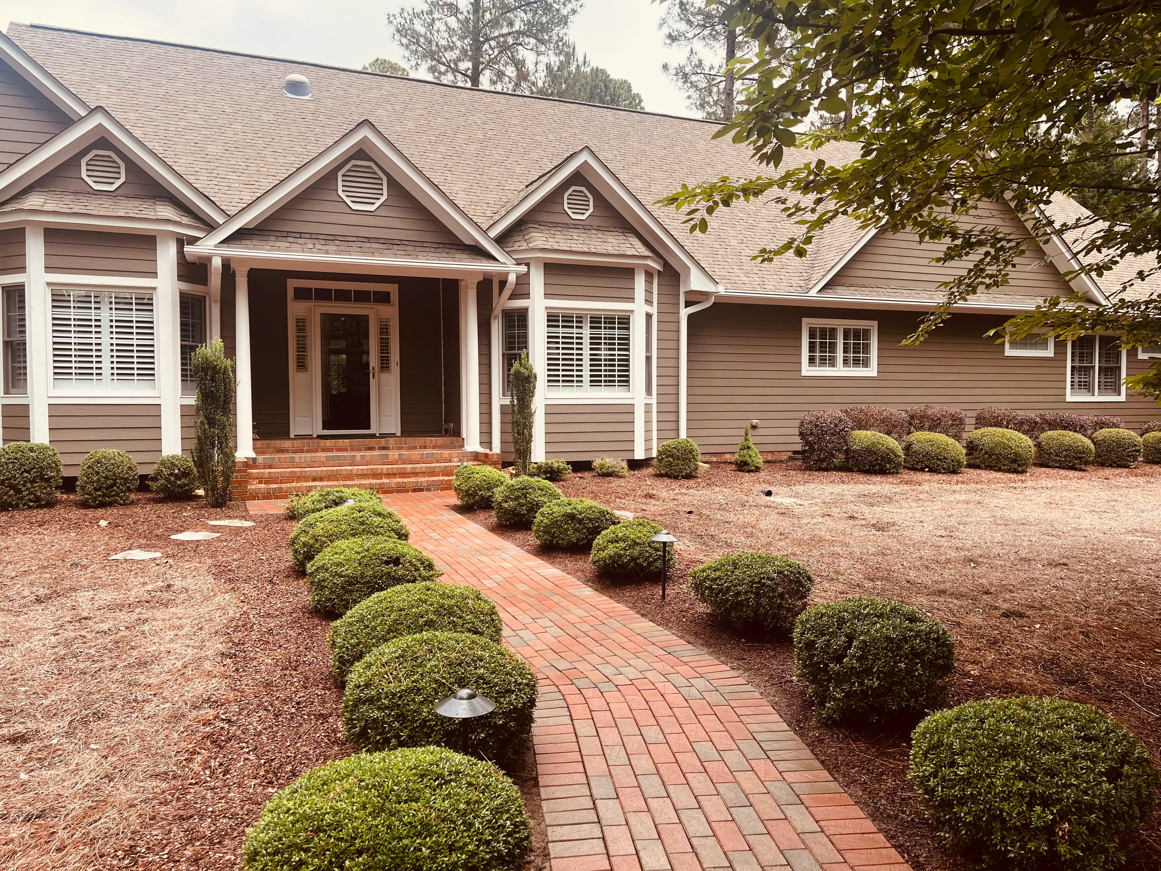 Clean brick walkway and shrubs in front of a Pinehurst home after pressure washing.