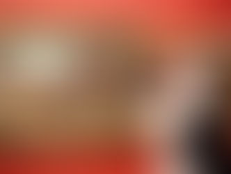 A newly married couple kisses in front of a vivid red wall displaying historic paintings. The mood is romantic and artful, with warm, rich colours.