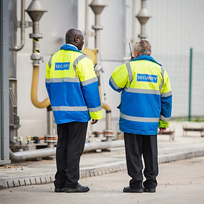Two security guards, backs to camera, one talking into walkie talkie
