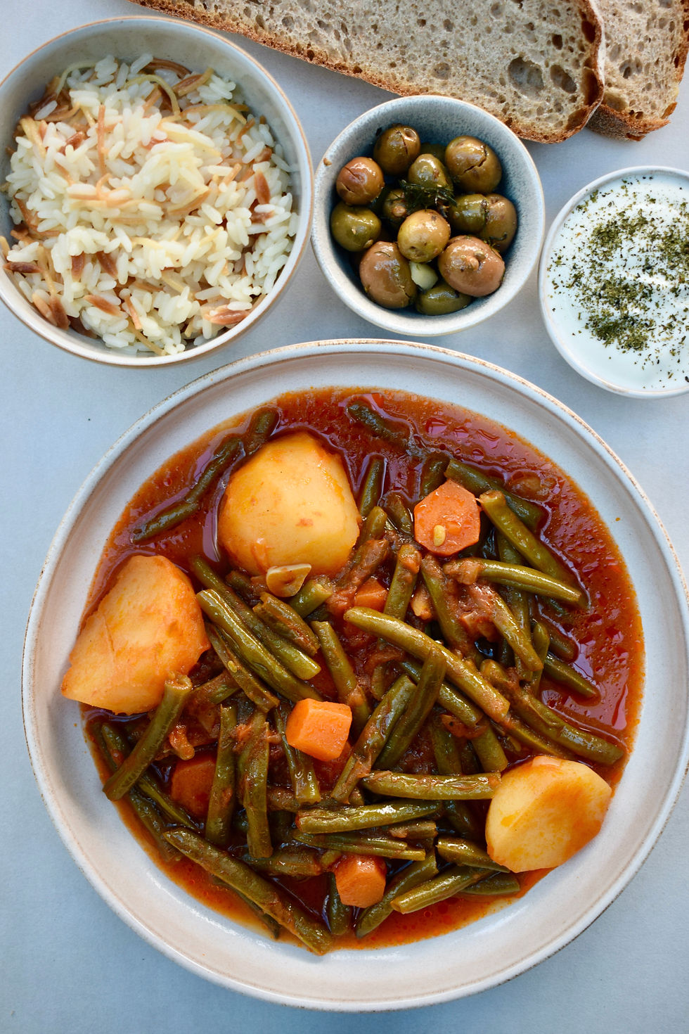 Prepared taze fasulye yahni served with rice, olives, yoghurt and bread