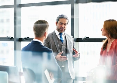 A businessman in a suit gestures while talking to colleagues.