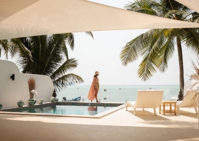 Woman in sun hat walking by a pool overlooking the ocean.