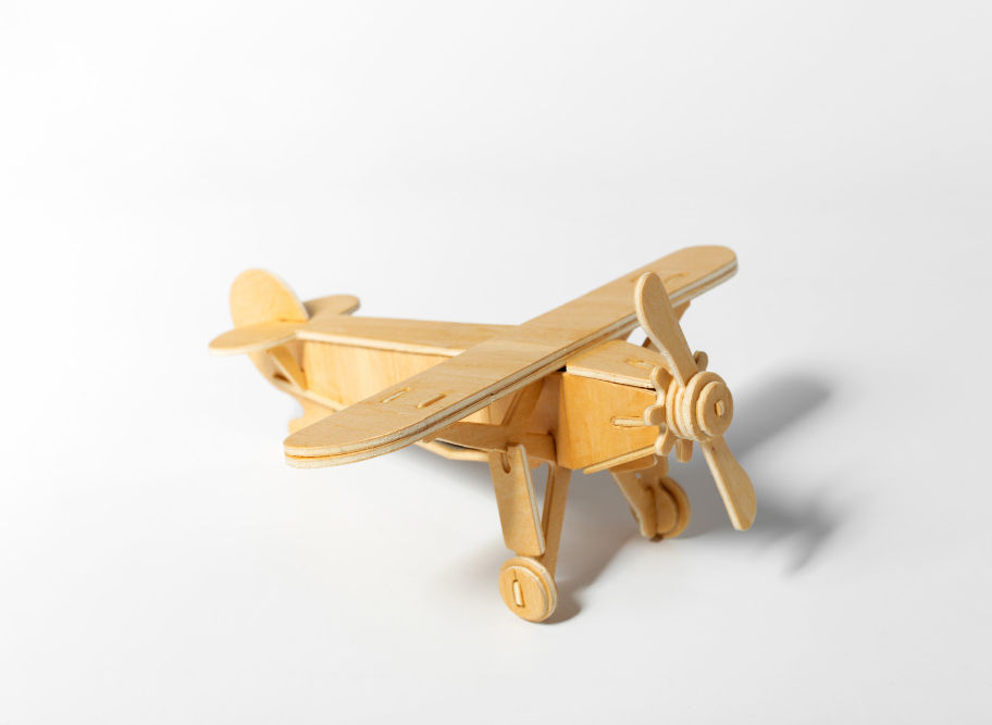 Wooden toy airplane sits on a white surface, ready to take flight.
