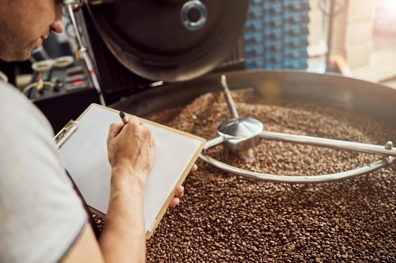 Person taking notes next to a coffee roaster filled with beans