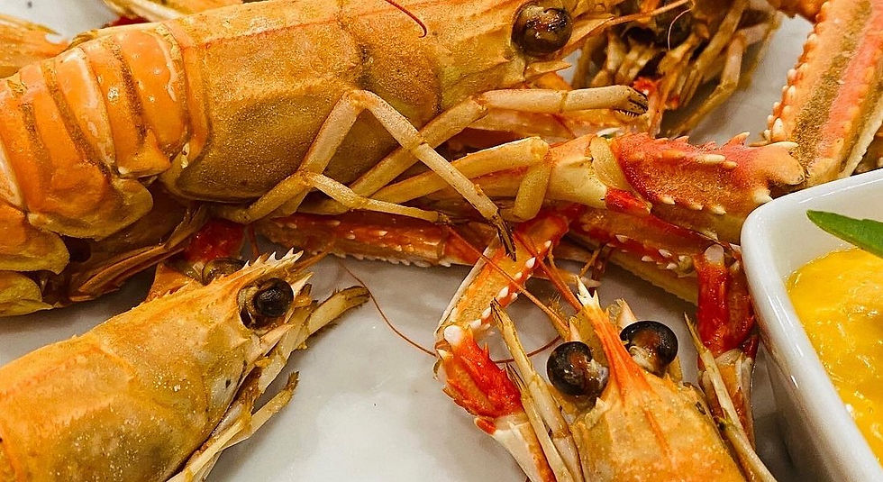 Close-up of orange scampi on a white plate with a side of yellow sauce. The scampi's eyes and claws are prominent. Vibrant seafood scene.