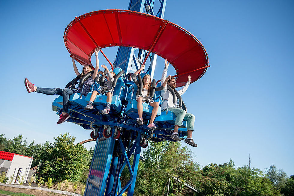 People on a blue and red amusement ride raise their arms, smiling. Clear sky and trees in the background create a joyful scene.