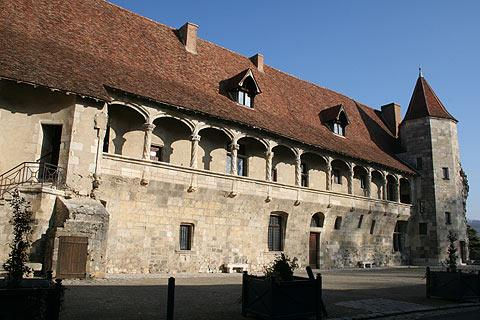 Historic stone building with arched balconies and red tile roof, set against a clear sky. A stone tower is visible on the right side.