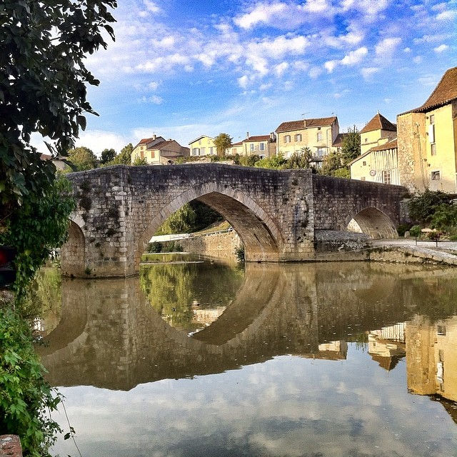 Charming stone bridge in Nérac gracefully spans the reflective waters, surrounded by picturesque houses and greenery.