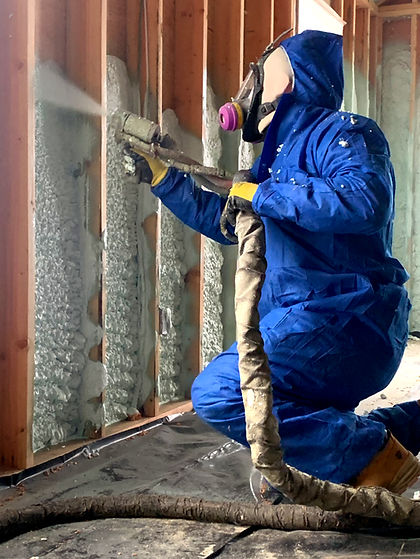 A divine energy solutions technition in a blue pull over suit and respirator applies spray foam insulation