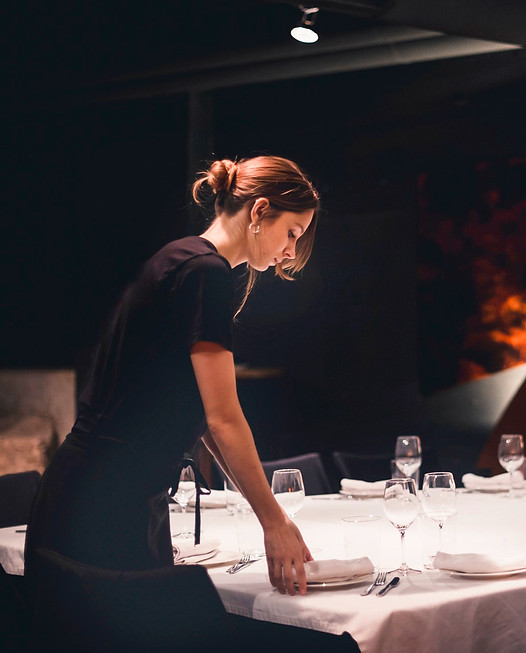 A server laying a table in a candlelit dining room before service