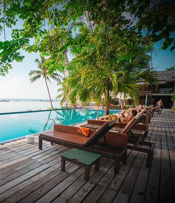 Sun loungers beside the pool at a tropical resort, shaded by palms