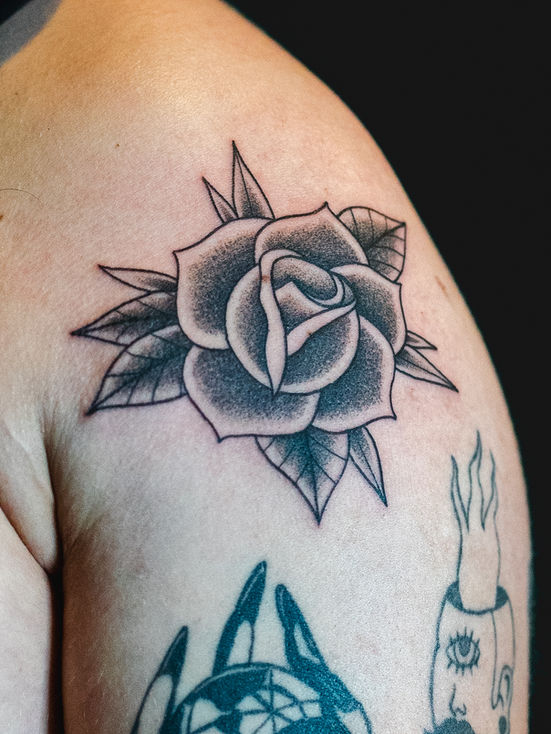 Traditionelles, schattiertes Tattoo einer Rose auf einer männlichen Schulter vor einem schwarzen Hintergrund