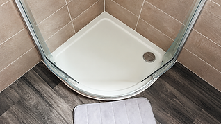 Modern shower area with glass door, beige tiles, and a window ledge with a potted plant.