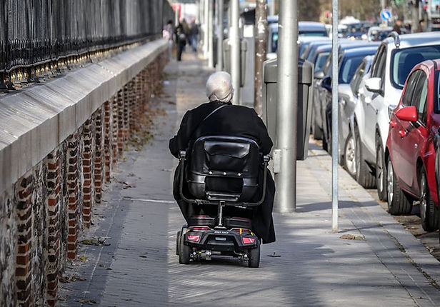 Person riding a black travel scooter on a sidewalk