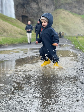 Toddler in a blue rain suit jumping in a puddle
