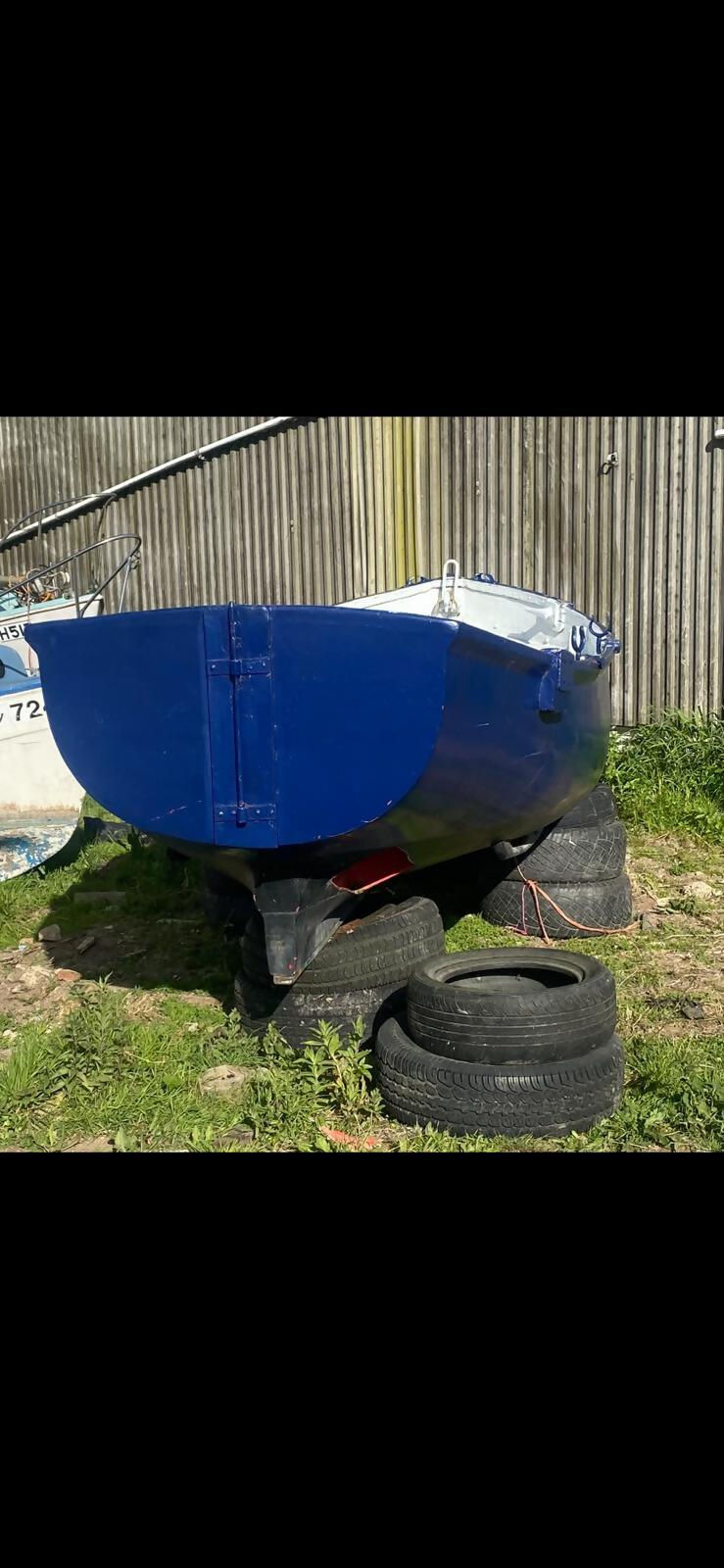 Small blue yacht on a trailer in a grassy yard
