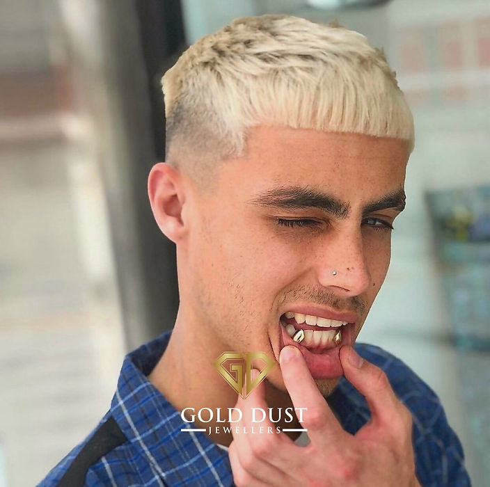 Young man winking, showing silver grillz, adjusting gold cap.