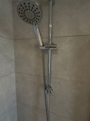Chrome shower head and hose mounted on a light-colored tiled wall