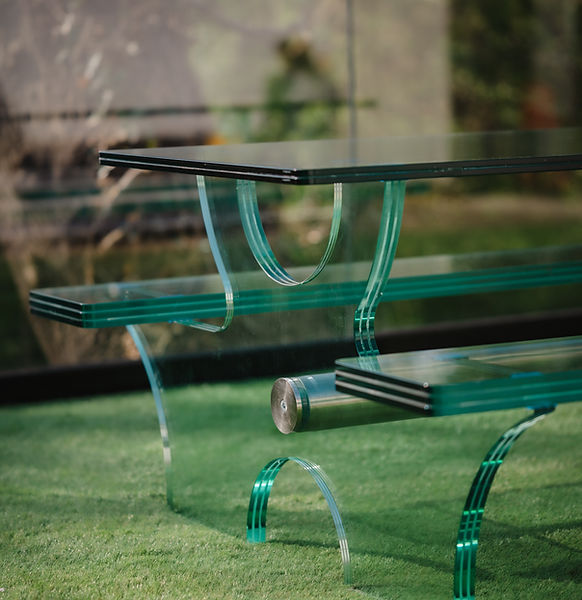 Bespoke glass picnic bench with polished metallic legs in a garden setting