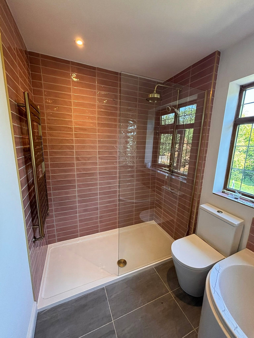 Modern bathroom with beige tiles, glass shower, white sink with wooden cabinetry, and a toilet under a large mirror.