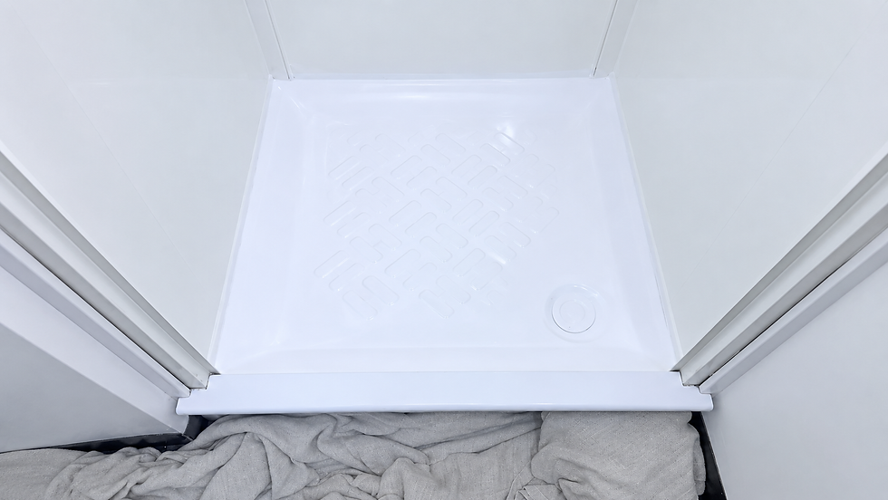 A plumber inspects a newly installed shower tray in a tiled bathroom.