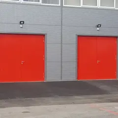 Two bright red steel doors on a grey industrial building.