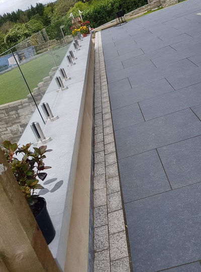 Paved path and wall with metal posts next to green grass.