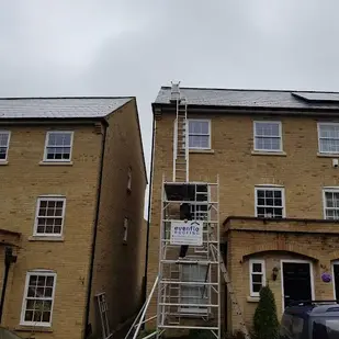 Scaffolding between two buildings with visible windows and doors under cloudy sky.