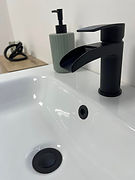 Bathroom fixtures and accessories in a flat lay, featuring brass taps, a white basin, and textured tile samples.