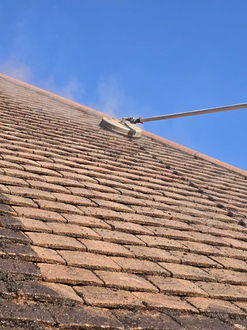 High-pressure roof cleaning on shingles under a blue sky.