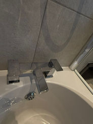 Modern chrome faucet over white bathtub with grey tiles