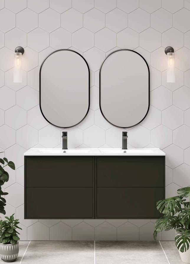 A man wearing a green shirt opens a wooden drawer under a bathroom sink in a modern, minimalist setting.