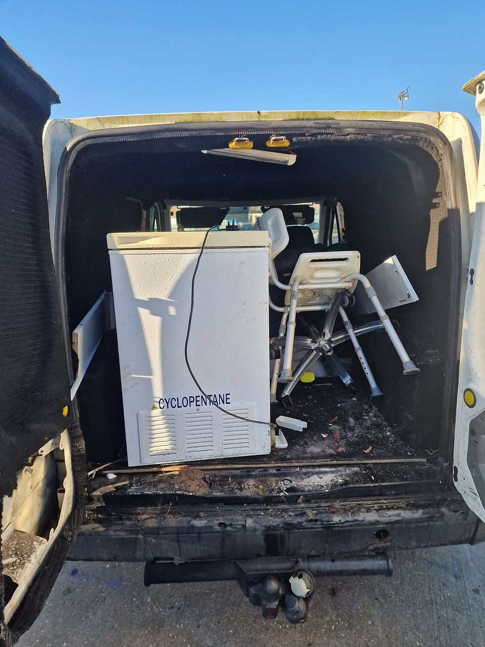 A woman wearing gloves loads a small cabinet into the back of a van alongside black bags.
